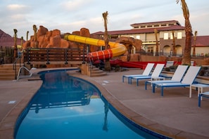 A pool area with a water slide, lounge chairs, and a building with a red-tiled roof.