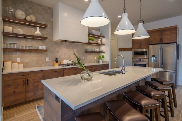 A modern kitchen with a large island, stainless steel appliances, wooden cabinets, and pendant lighting.