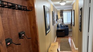 A hallway with wooden flooring, a bench, a door with a coat rack, and framed pictures on the walls.
