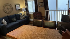 A living room with a ceiling fan, a sofa, a coffee table, and a view of a snowy landscape through large windows.