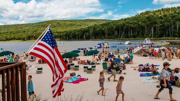 A beach with an American flag, people, and beach chairs.