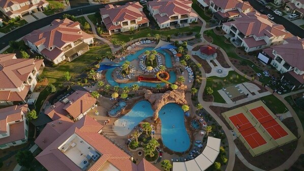 Vista aérea de una zona residencial con casas, un complejo de piscinas y canchas de tenis.