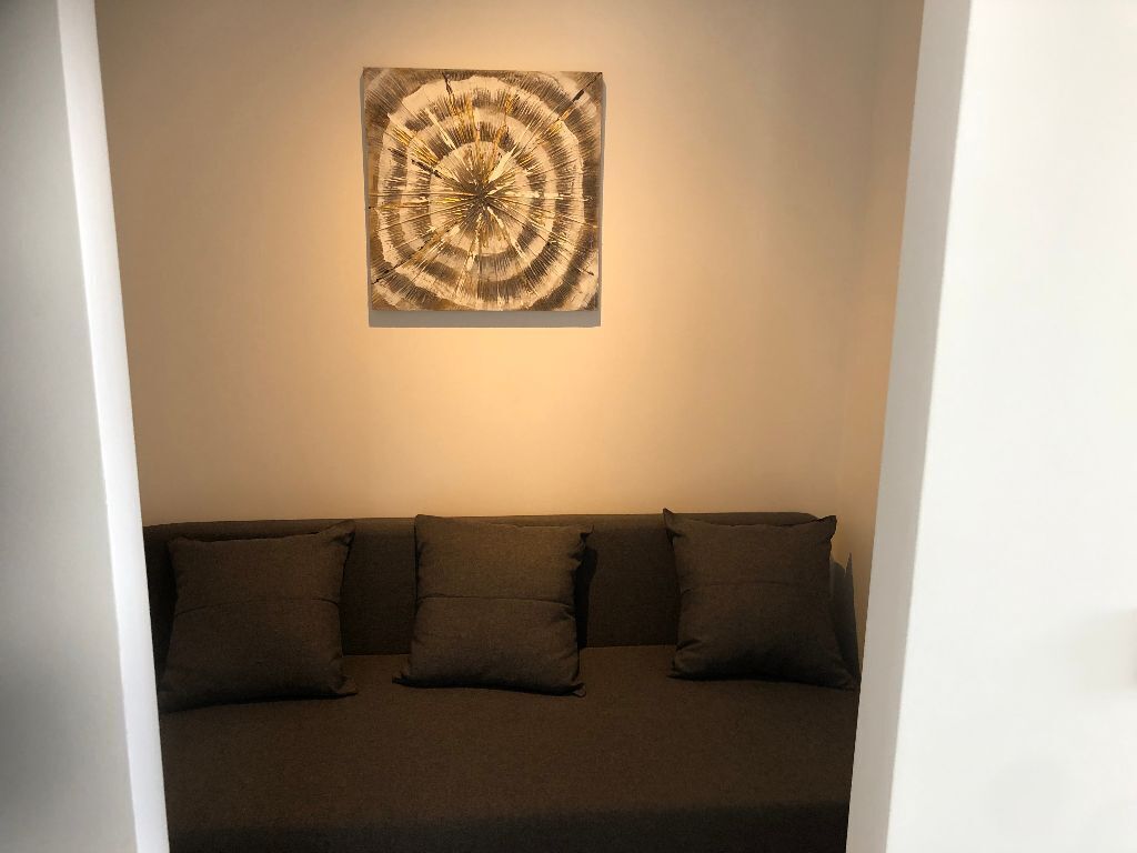 Une pièce dont le canapé est de couleur foncée et qui est placé contre un mur blanc, avec une œuvre d’art circulaire accrochée au-dessus.