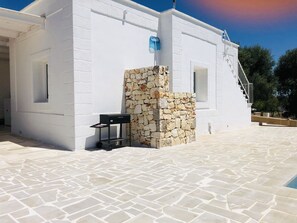 A white building with a stone wall, a black cart, and a staircase leading to a door.
