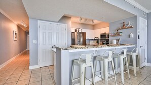 A kitchen with a central island, bar stools, a refrigerator, and a microwave.