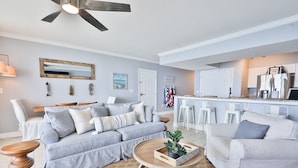 A living room with a sofa, coffee table, and a kitchen area with bar stools.