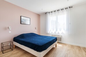 A bedroom with a bed, a window with sheer curtains, a picture on the wall, and a small bedside table.