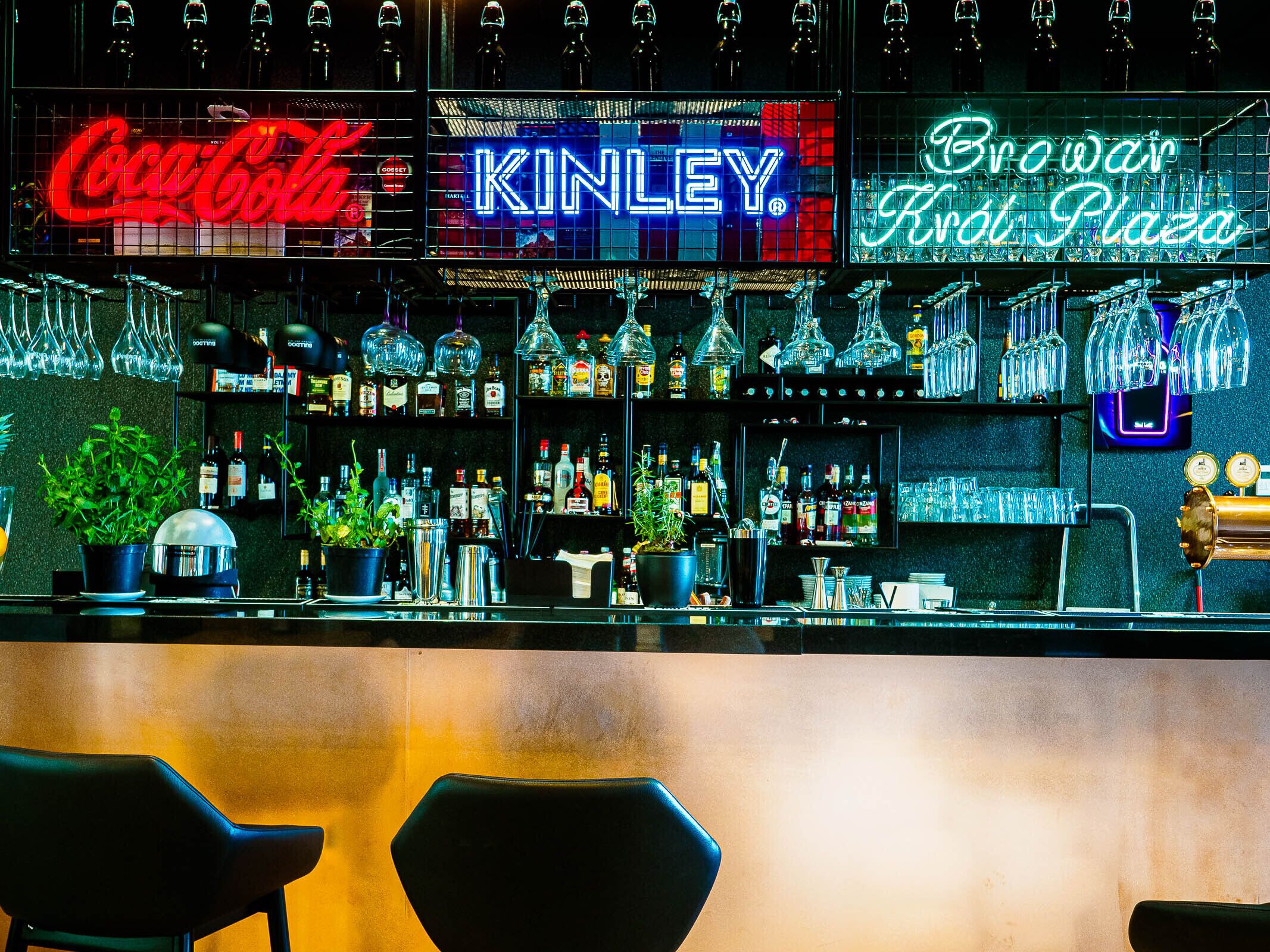 A bar with neon signs for Coca-Cola, Kinley, and Browar Kral Plaza.