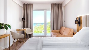 A hotel room with a bed, a desk, a chair, a table, a lamp, and a view of the outdoors. - Resort Król Plaza Spa & Wellness (Postomino)