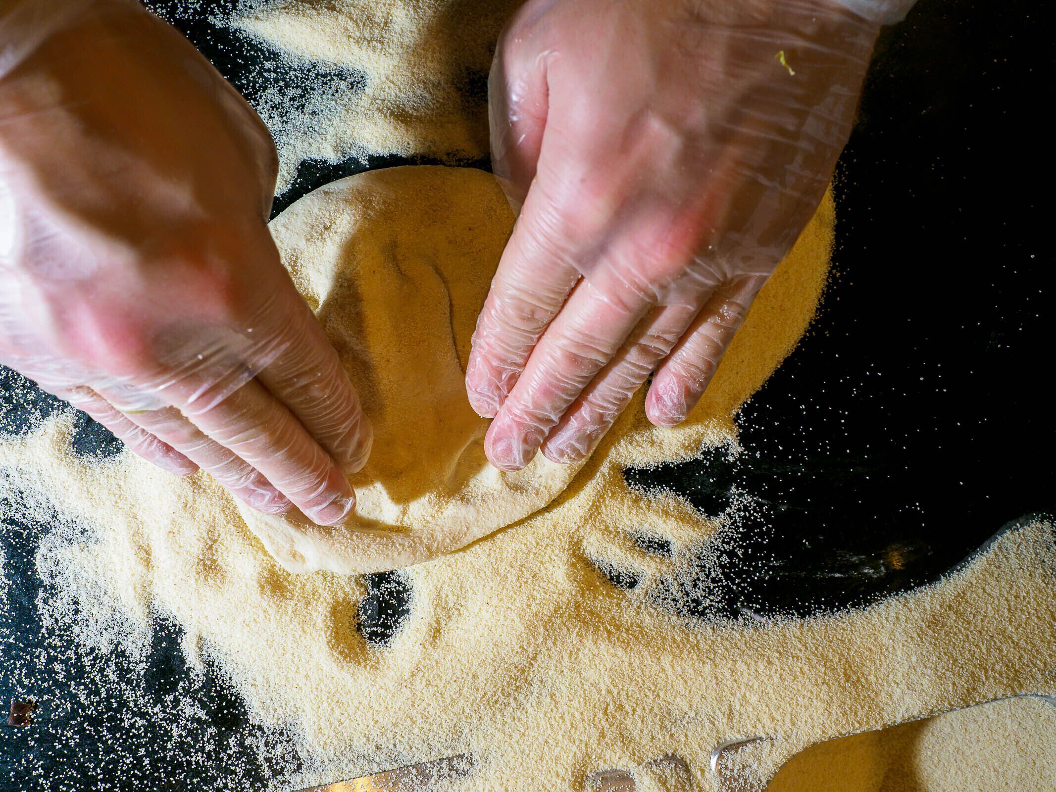 Hands shaping dough on a surface with flour scattered around.
