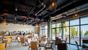 A modern restaurant with a spacious dining area, large windows, and a visible kitchen in the background. - Resort Król Plaza Spa & Wellness (Postomino)