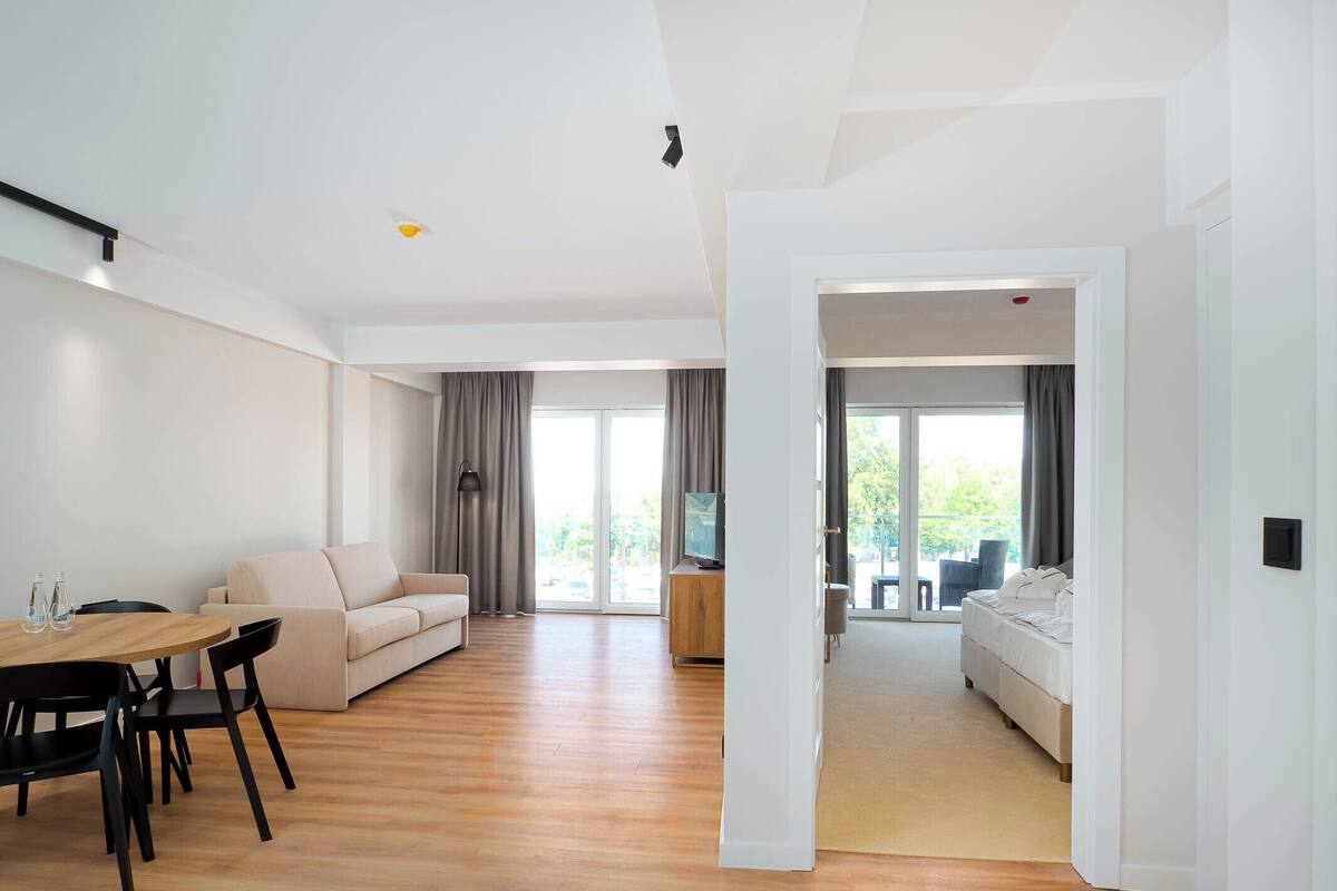 A modern living room with a wooden floor, a sofa, a dining table with chairs, and a TV.