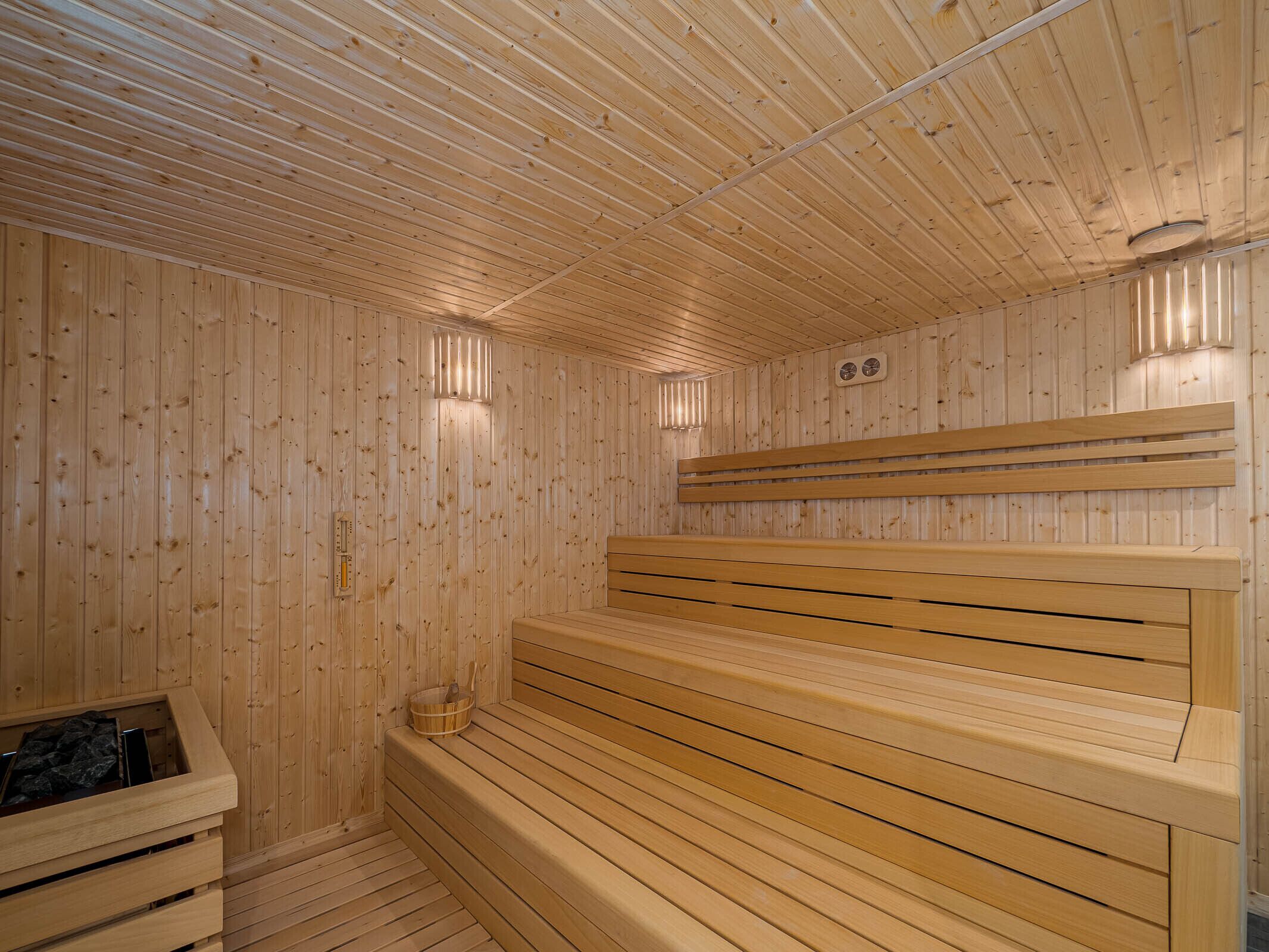 A wooden sauna with benches and a bench seat, a wooden wall, and a small heater.