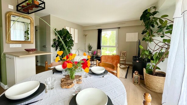 A dining area with a round table set for four, surrounded by chairs. There is a large potted plant to the right and a hanging plant above the table. - L'Artistik - Appt avec Balcon et parking (Vannes)