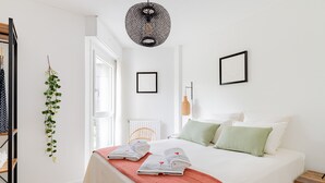 A bedroom with a bed, pillows, a bedside table, a hanging plant, and a ceiling light fixture. - L'Artistik - Appt avec Balcon et parking (Vannes)