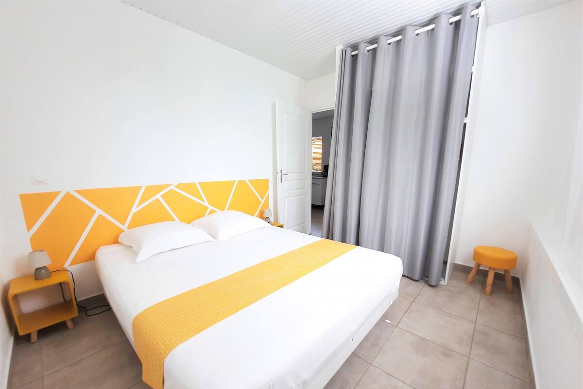 A hotel room with a large bed, a nightstand, a small stool, and a bathroom visible through a door.