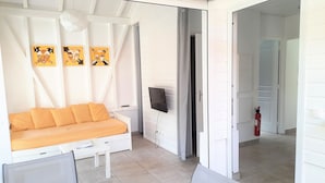 Une pièce avec un canapé blanc, un téléviseur fixé au mur et un extincteur près de la porte.