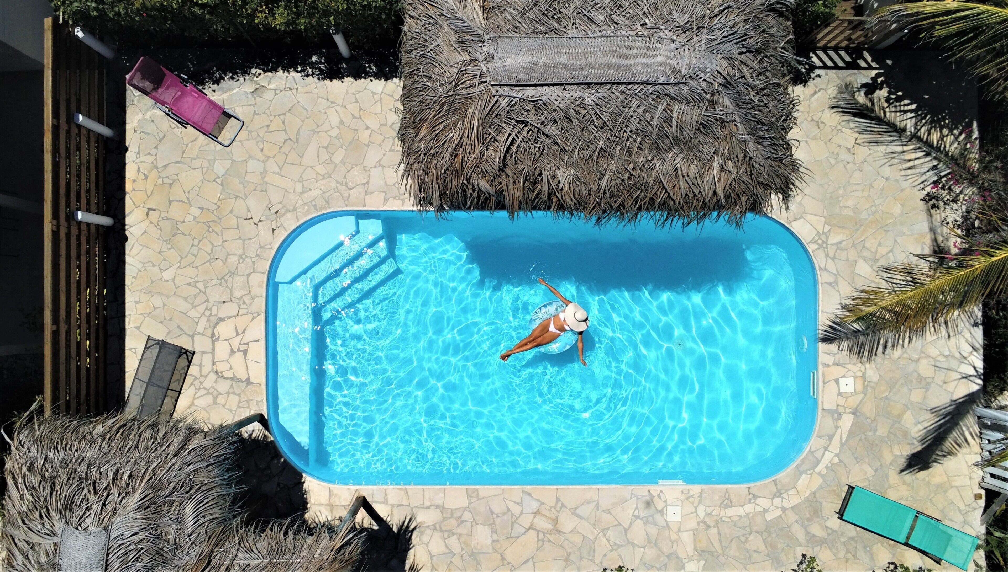 An aerial view of a swimming pool surrounded by stone tiles, with a person swimming.
