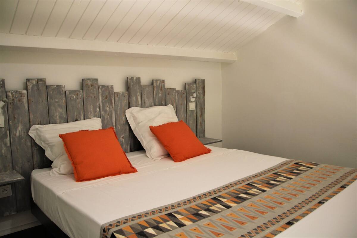A bed with white bedding, two orange pillows, and a patterned throw.