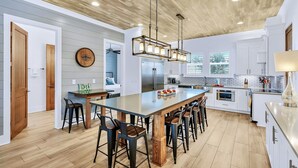 Una cocina moderna con una isla grande, taburetes de bar, un refrigerador y un techo de madera.