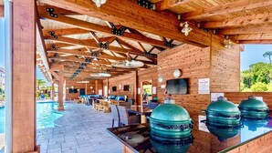 Un espacio al aire libre cubierto con piscina, asientos de madera y parrillas de barbacoa.