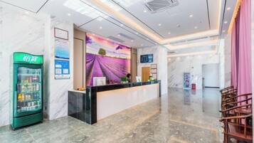 Zona d'entrada d'un hotel amb terra de marbre, taulell de recepció, màquina expenedora verda i un mural gran a la paret.