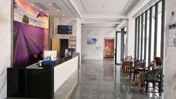 A hotel reception area with a reception desk, seating area, and a large window.