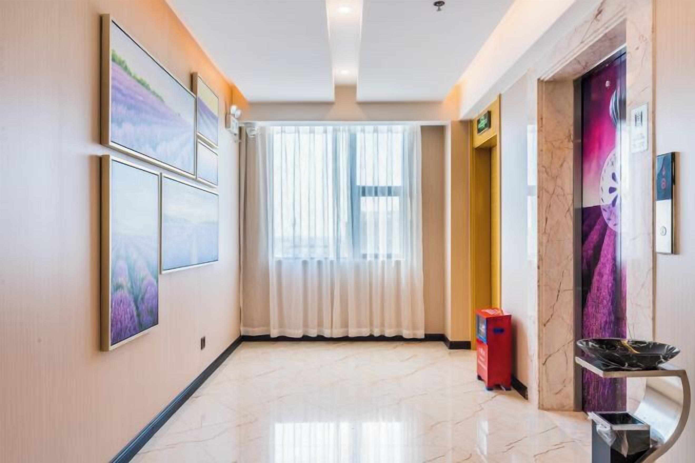 A hotel corridor with framed pictures on the walls, a red trash bin, and a door with a purple mural.
