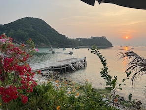 A pier extending into a calm body of water with boats, surrounded by lush greenery and flowering plants. - NAM DU PALACE (Kien Hai)