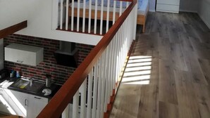 Un dormitorio tipo loft con techo inclinado, una ventana pequeña, una cama, una mesita de noche y un aparador.