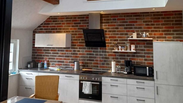 Una cocina moderna con un revoque de ladrillo, armarios blancos y una mesa de comedor de madera con sillas.