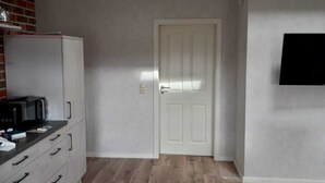 Un espacio habitable compacto con kitchenette, una puerta y televisor montado en la pared.