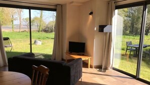 A modern room with a large window, a sofa, a TV, and a dining table. - Petite Maison - Piscine & Vue mer Grange Ouest (Locoal-Mendon)