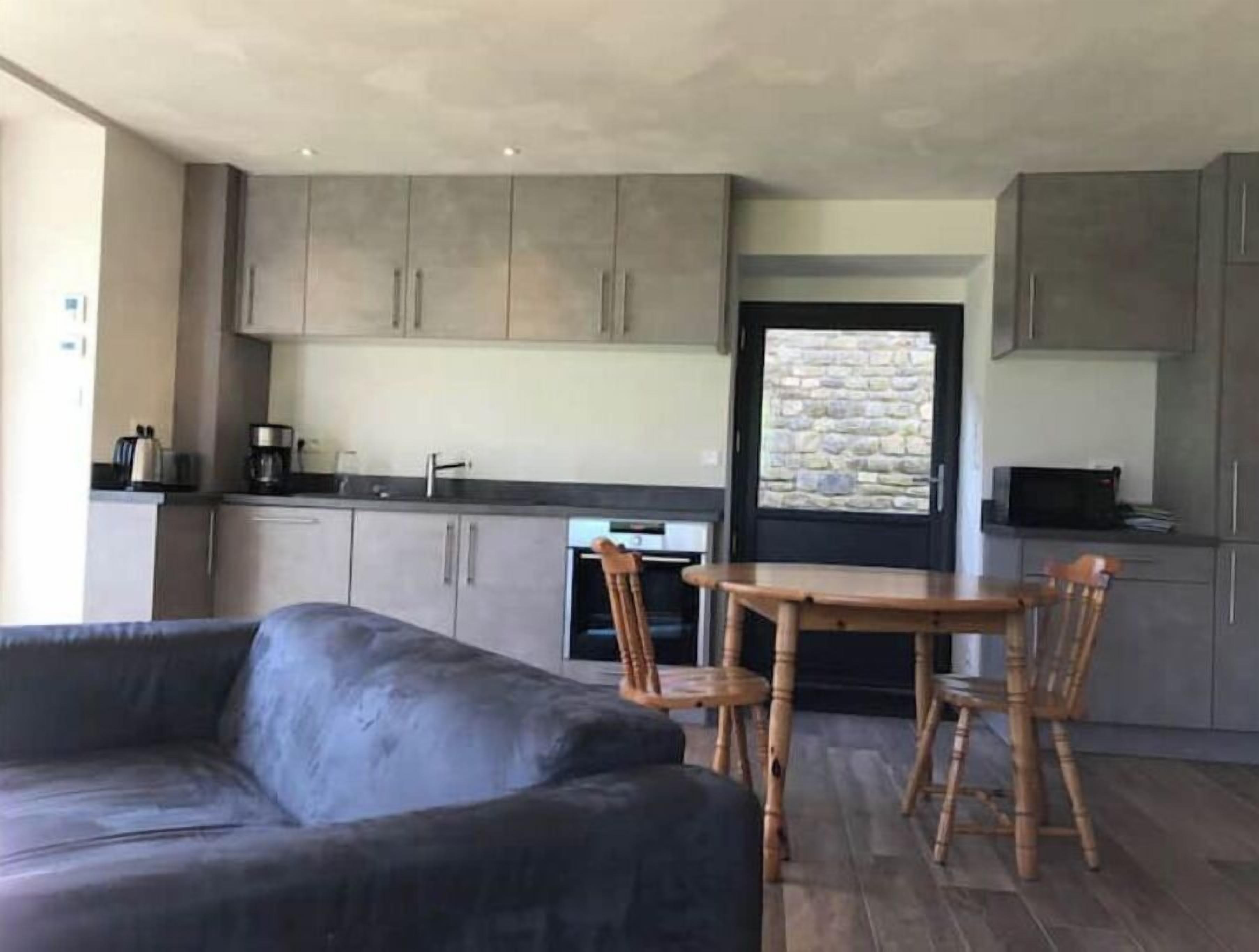 A modern kitchen with grey cabinets, a dining table with four chairs, and a black sofa.