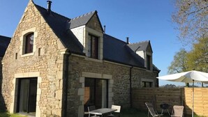 A stone building with a sloped roof, a door, and a small window. There is a table and chairs outside. - Petite Maison - Piscine & Vue mer Grange Ouest (Locoal-Mendon)