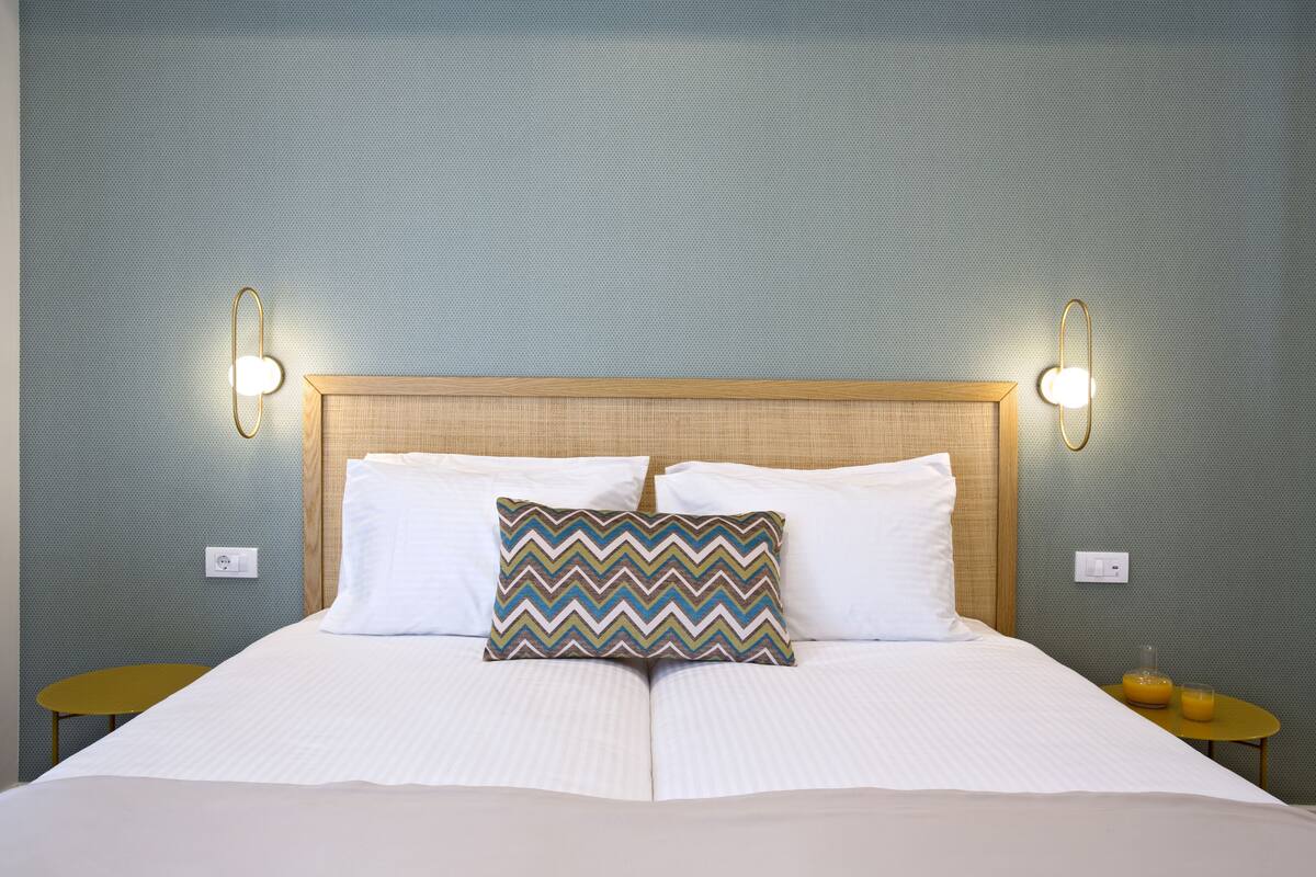 A neatly made bed with two pillows, a patterned pillow, and two wall-mounted lights.