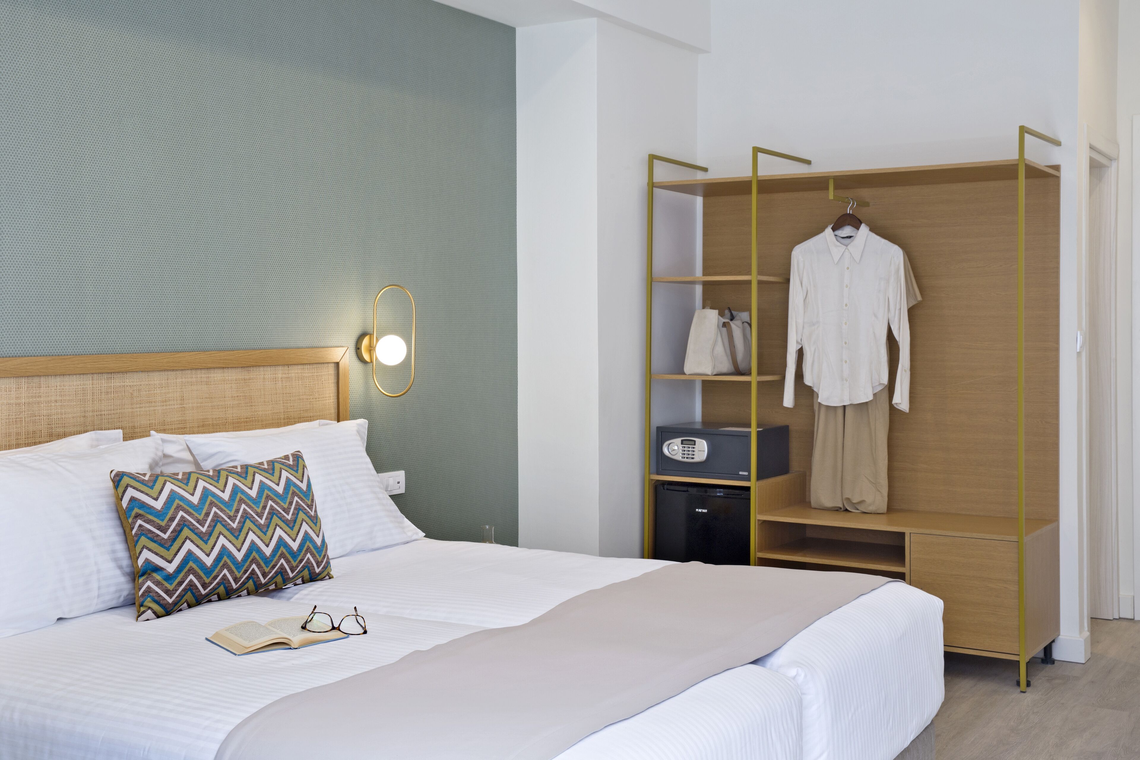 A neatly made bed with a pillow, a bedside table with a lamp, and a wardrobe with a hanging garment.