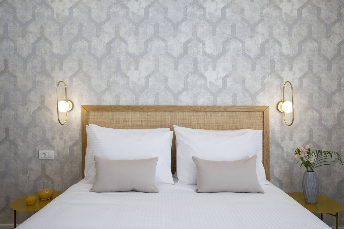 A neatly made bed with two pillows, a bedside table with a glass of orange juice, and a vase with flowers.