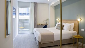 A modern hotel room with a large bed, a bedside table with a lamp, a view of the city through the window, and a balcony with a chair. - Hypnos Inn Athens (Athens)