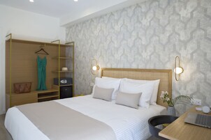 Quarto de hotel bem arrumado com uma cama grande, um guarda-roupa de madeira, uma escrivaninha com um laptop e uma parede com padrão geométrico.
