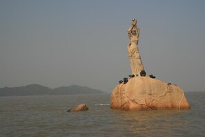 A large rock with a statue on top, surrounded by water. - Longxiang Hotel (Zhuhai)