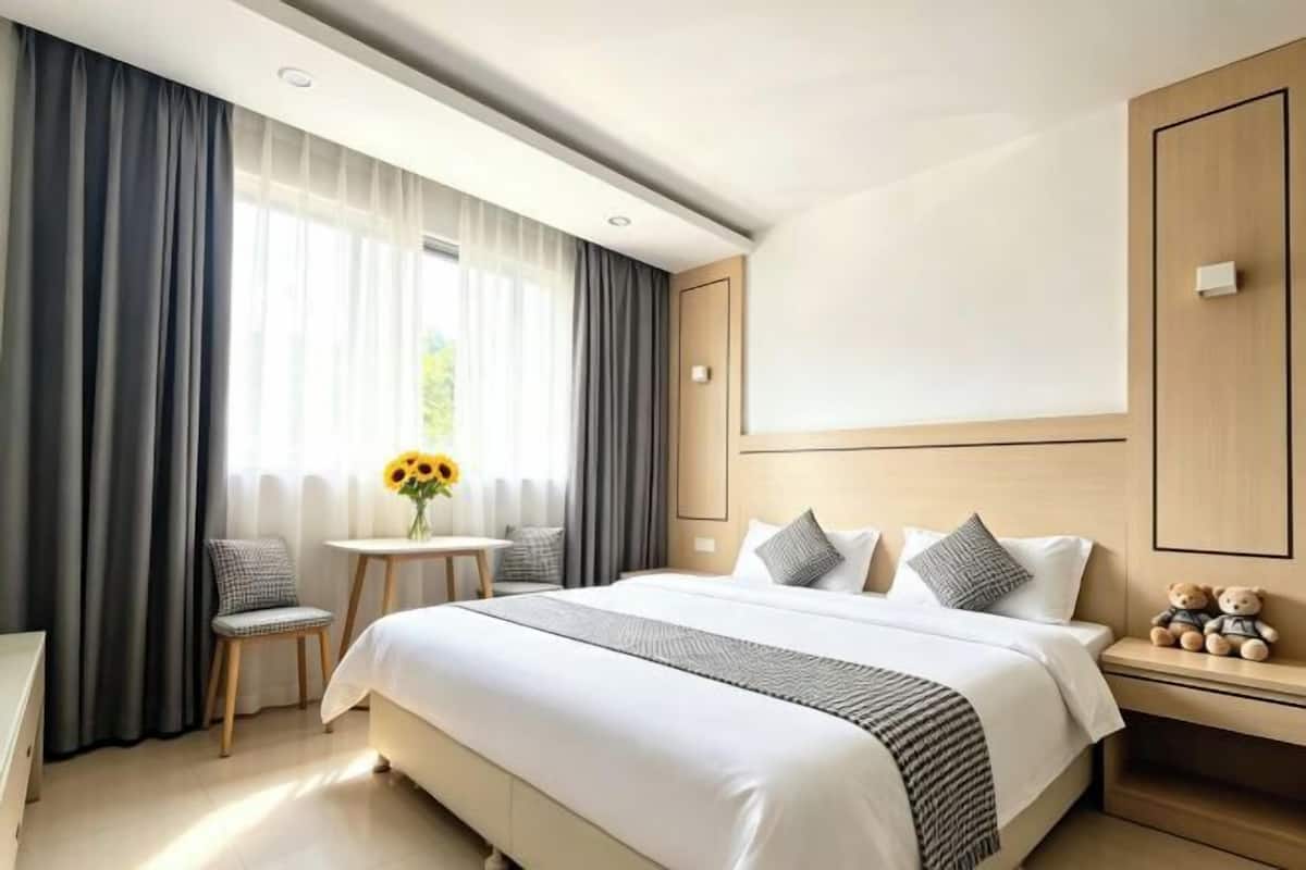 A hotel room with a large bed, a small table with a vase, and a nightstand with a teddy bear.