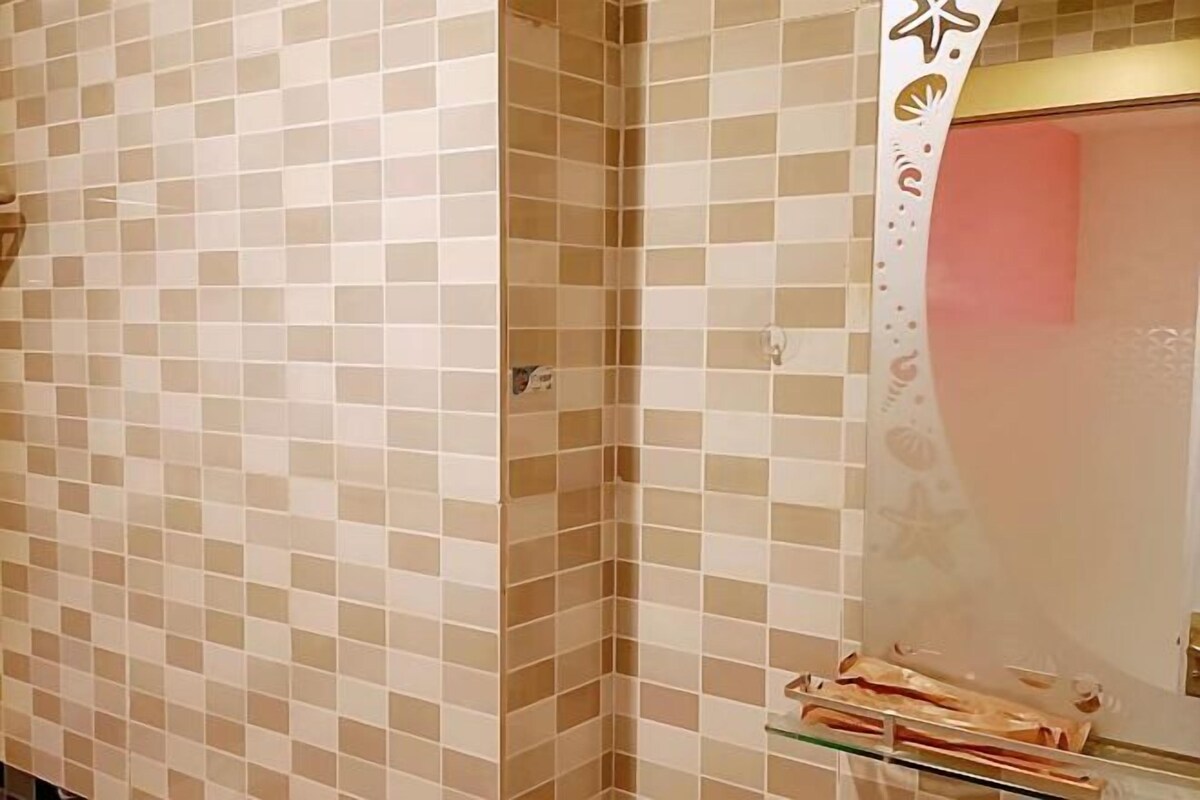 A bathroom with beige and white checkered tiles, a glass shelf with toiletries, and a towel rack.