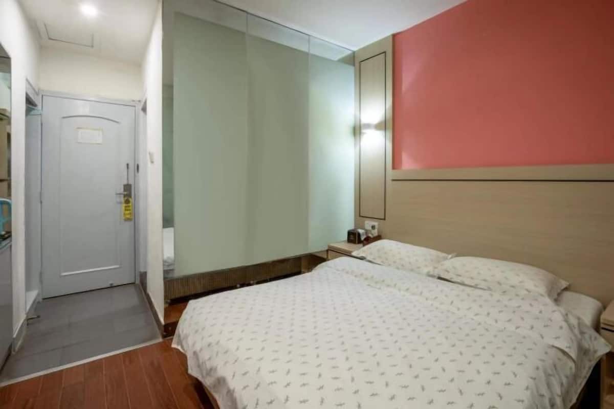 A hotel room with a bed, a bedside table, a mirror, and a door.