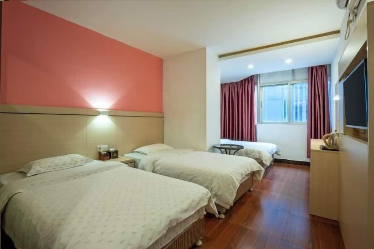 A hotel room with three beds, a small table, a TV, and a window with curtains.