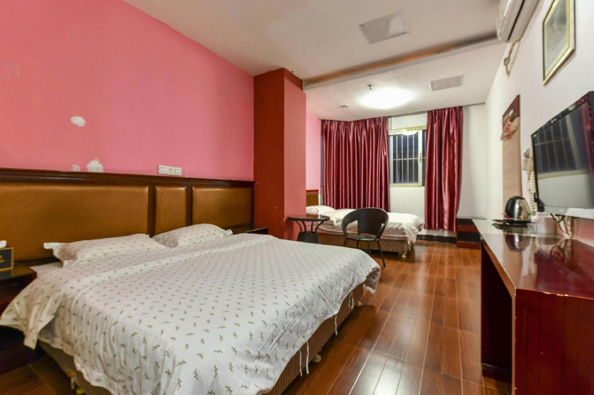 A hotel room with two beds, a desk, a chair, a television, and a window with curtains.