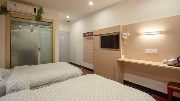A hotel room with two beds, a desk with a chair, a small window, a wall-mounted phone, and an air conditioning unit. - Longxiang Hotel (Zhuhai)
