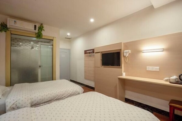 Habitación de hotel con dos camas, un escritorio y una silla, un ventanal pequeño, un teléfono en la pared y un equipo de aire acondicionado.