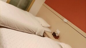 A bed with white bedding and pillows, a bedside table with a tissue box and a small item on it, and a red wall in the background. - Longxiang Hotel (Zhuhai)
