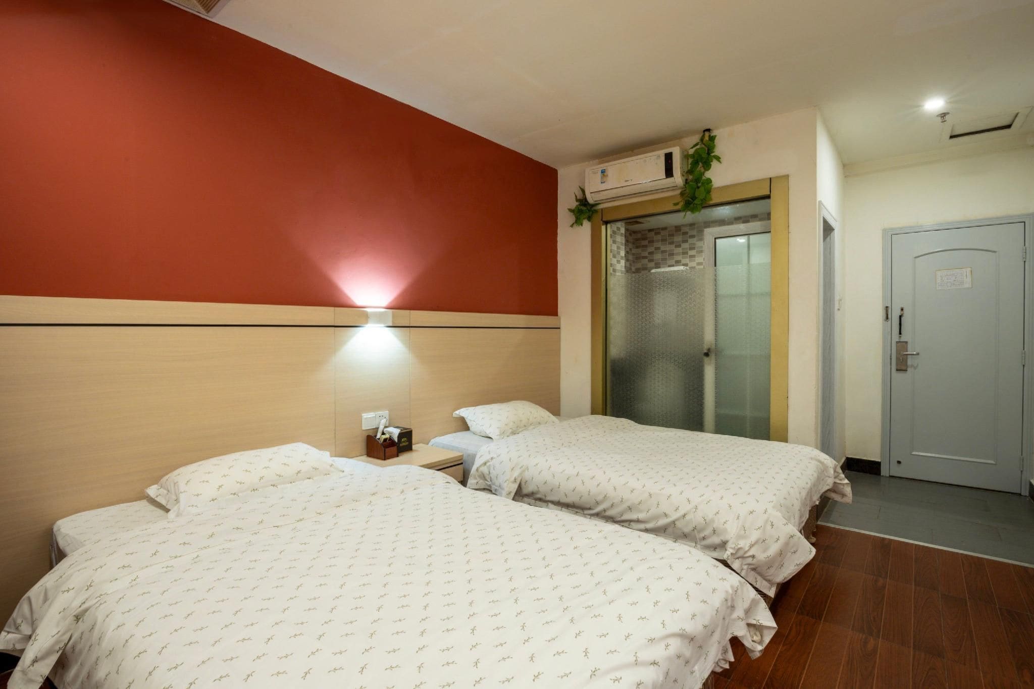 A hotel room with two beds, a wall-mounted air conditioner, and a door with a lock.